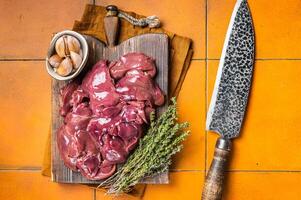 Raw chicken liver, fresh fowl giblets on wooden board. Orange background. Top view photo