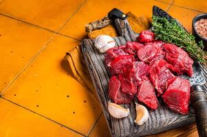 Raw beef meat chopped in cubes on wooden cutting board for cooking stew. Orange background. Top view. Copy space photo