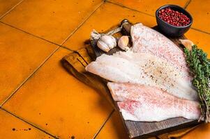 Uncooked ocean red perch fillet, redfish with herbs and spices. Orange background. Top view. Copy space photo