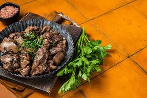 Roast chicken liver with onions and herb in a steel plate. Orange background. Top view. Copy space photo