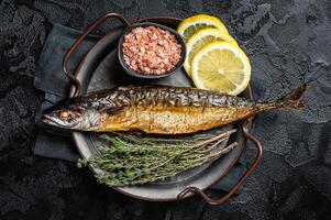 Baked Mackerel Scomber fish in steel tray with thyme and lemon. Black background. Top view photo