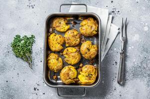 Broken potatoes baked with rosemary and thyme. Gray background. Top view photo