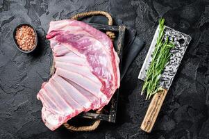 Butcher table with Rack of lamb, raw mutton ribs with meat cleaver. Black background. Top view photo
