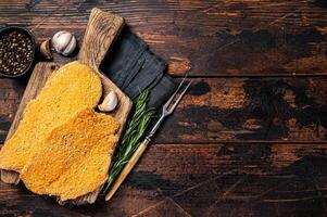 Uncooked Wiener schnitzel in breadcrumbs, raw pork meat. Wooden background. Top view. Copy space photo