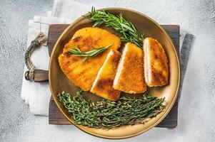 Chicken fried Cordon bleu cutlet with ham and cheese on a plate with herbs. White background. Top view photo