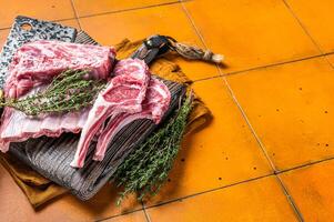 Raw lamb meat chops cutlets on butcher cutting board. Orange background. Top view. Copy space photo
