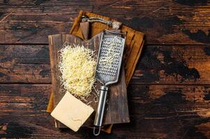 Piece of semi hard cheese and grated cheese with grater. Wooden background. Top view photo