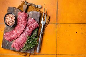 Butcher table with Raw lamb tenderloin Fillet, Mutton loin Meat with thyme. Orange background. Top view. Copy space photo