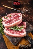 Raw fresh saddle of lamb mutton with herbs and spices on butcher board. Dark background. Top view photo