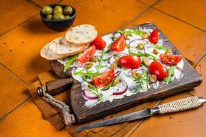 Trendy Butter Board with olives, onion, arugula, capers and tomato, Butterboard. Orange background. Top view photo