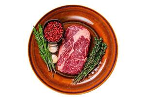 Black angus rib eye raw beef steak on a rustic plate. Isolated, white background. Top view. photo