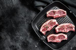 Raw lamb loin rib chops steaks in grill skillet with rosemary and thyme. Black background. Top view. Copy space photo