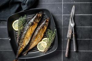 Grilled mackerel fish with lemon, herbs and spices in a skillet. Black background. Top view photo