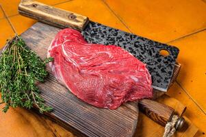 Piece of Raw beef meat for stew with herbs on butcher cutting board. Orange background. Top view photo