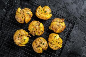 Crushed, smashed potatoes baked with rosemary and thyme. Black background. Top view photo