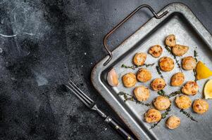 Scallops poached in a butter and garlic Sauce in a steel tray with thyme. Black background. Top view. Copy space photo