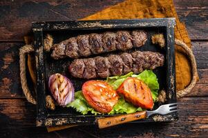 Traditional middle east kefta or kofta kebab, ground beef and lamb meat grilled on skewers served with tomato, salad and onion. Wooden background. Top view photo