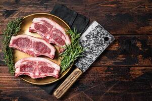 Uncooked Raw lamb loin chops steaks, saddle in plate with rosemary and thyme. Wooden background. Top view. Copy space photo
