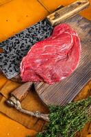 Piece of Raw beef meat for stew with herbs on butcher cutting board. Orange background. Top view photo