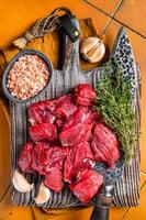 Raw beef meat chopped in cubes on wooden cutting board for cooking stew. Orange background. Top view photo