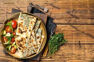 Gozleme flatbread with greens and vegetable salad on garnish. Wooden background. Top view. Copy space photo