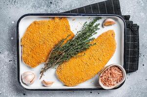 Cooking raw chicken schnitzel in breadcrumbs, uncooked meat steak. Gray background. Top view photo