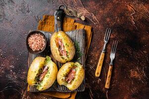 Jacket potatoes baked with cheese, herbs and butter. Dark background. Top view photo