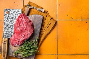 Piece of Raw beef meat for stew with herbs on butcher cutting board. Orange background. Top view. Copy space photo