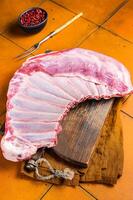 Raw rack of lamb mutton ribs on butcher board with spices. Orange background. Top view photo