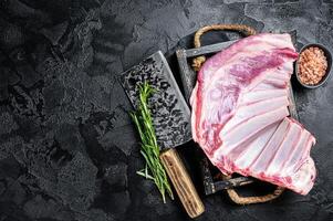 Butcher table with Rack of lamb, raw mutton ribs with meat cleaver. Black background. Top view. Copy space photo