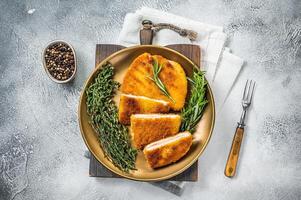 Chicken fried Cordon bleu cutlet with ham and cheese on a plate with herbs. White background. Top view photo