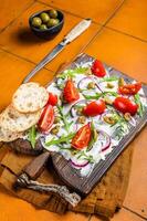 Trendy Butter Board with olives, onion, arugula, capers and tomato, Butterboard. Orange background. Top view photo