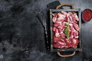 Uncooked Bird offals, raw chicken giblets, gizzards, stomachs, liver and hearts in a wooden tray. Black background. Top view. Copy space photo