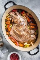 Braised lamb mutton shoulder in a baking dish with vegetables in red wine. White background. Top view photo