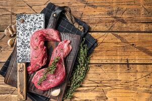 Raw Sirloin flap or Bavette raw beef meat steak on a wooden butcher board with meat cleaver. Wooden background. Top view. Copy space photo