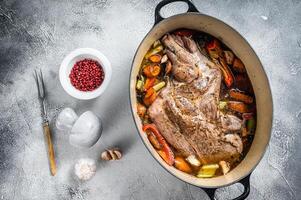 Braised lamb mutton shoulder in a baking dish with vegetables in red wine. White background. Top view photo