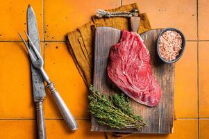 Piece of Raw beef meat for stew with herbs on butcher cutting board. Orange background. Top view photo
