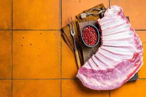 Raw rack of lamb mutton ribs on butcher board with spices. Orange background. Top view. Copy space photo