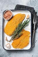 Cooking raw chicken schnitzel in breadcrumbs, uncooked meat steak. Gray background. Top view photo