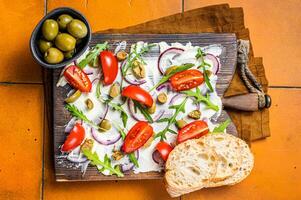 Trendy Butter Board with olives, onion, arugula, capers and tomato, Butterboard. Orange background. Top view photo