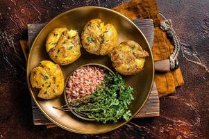 Crushed, smashed potatoes baked with rosemary and thyme on plate. Dark background. Top view photo