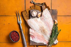 Uncooked ocean red perch fillet, redfish with herbs and spices. Orange background. Top view photo