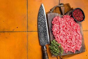 Fresh Raw Mince, Ground beef and pork meat on a butcher board. Orange background. Top view. Copy space photo