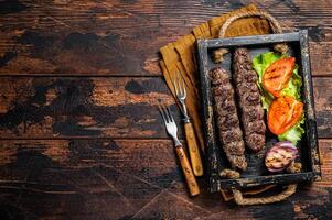 Traditional middle east kefta or kofta kebab, ground beef and lamb meat grilled on skewers served with tomato, salad and onion. Wooden background. Top view. Copy space photo