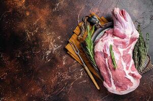 Mutton lamb whole shoulder, raw meat in a steel tray with herbs. Dark background. Top view. Copy space photo