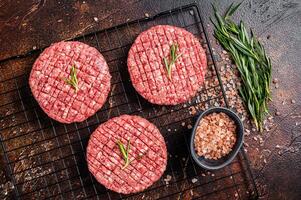 Raw burger cutlet from beef meat with spices and rosemary ready for cooking. Dark background. Top view photo