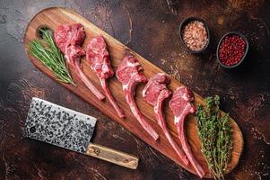 Raw Lamb chop steak on butcher board with rosemary and thyme. Dark background. Top view photo