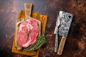 Fresh Marbled Rib eye steak with herbs on butcher cutting board, raw beef meat. brown background. top view photo