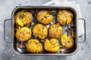 Broken potatoes baked with rosemary and thyme. Gray background. Top view photo