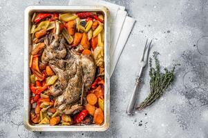 Roast lamb mutton shoulder meat in a baking dish with vegetables. Gray background. Top view photo